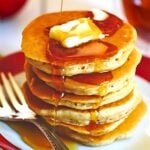A stack of apple cinnamon pancakes on a plate with slices of butter and maple syrup on them.