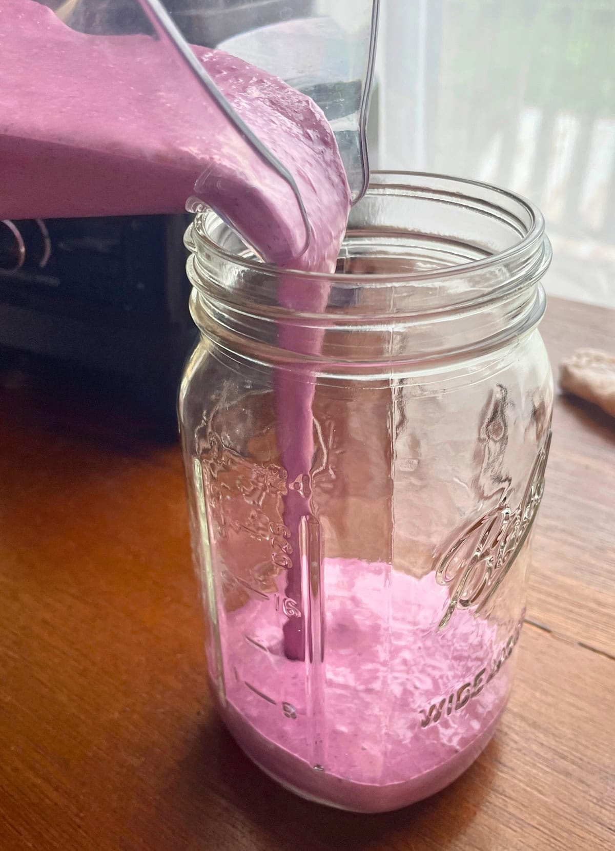Blueberry pineapple smoothie being poured from a blender into a large mason jar.