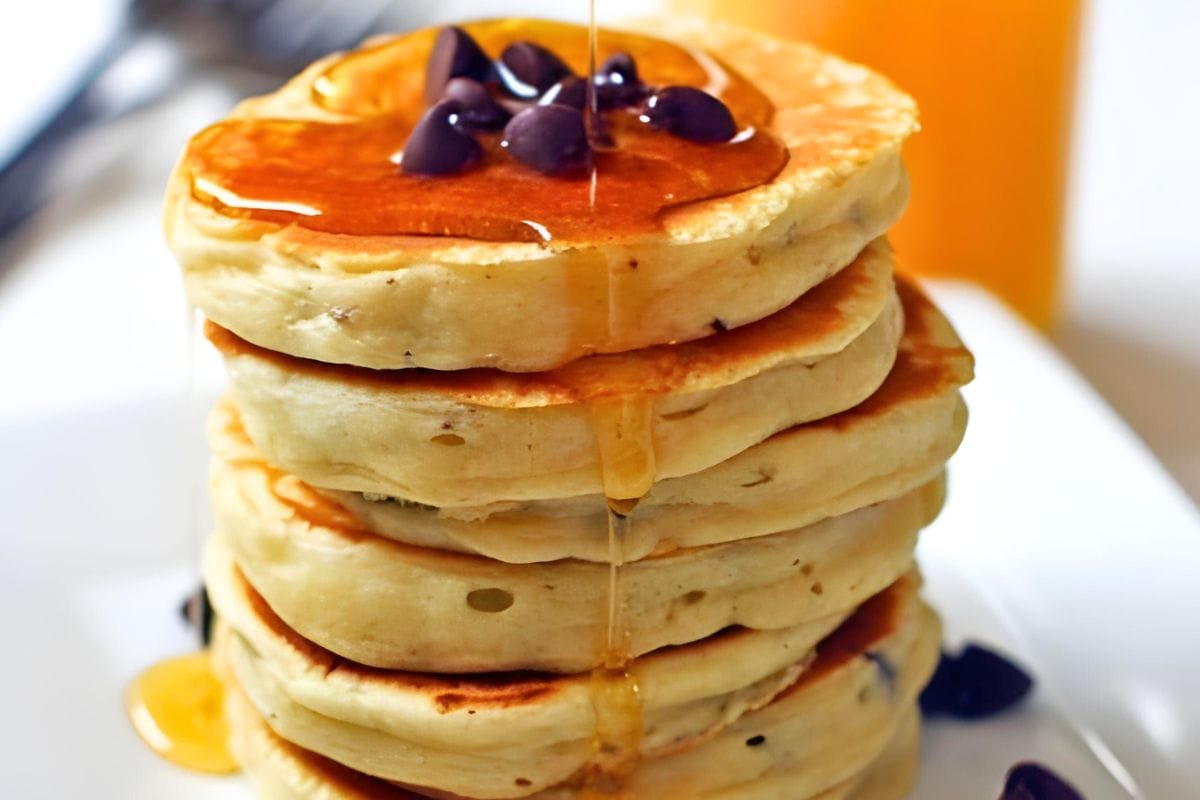 A stack of fluffy chocolate chip pancakes with maple syrup drizzled on them.