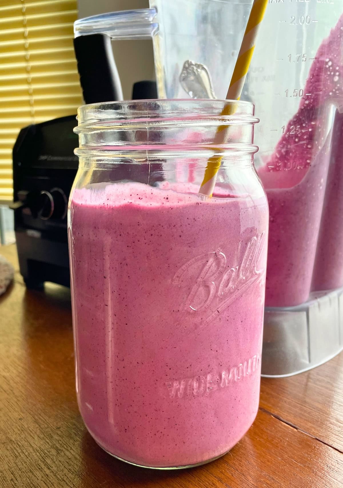 A blueberry pineapple smoothie poured into a large mason jar with a yellow straw.
