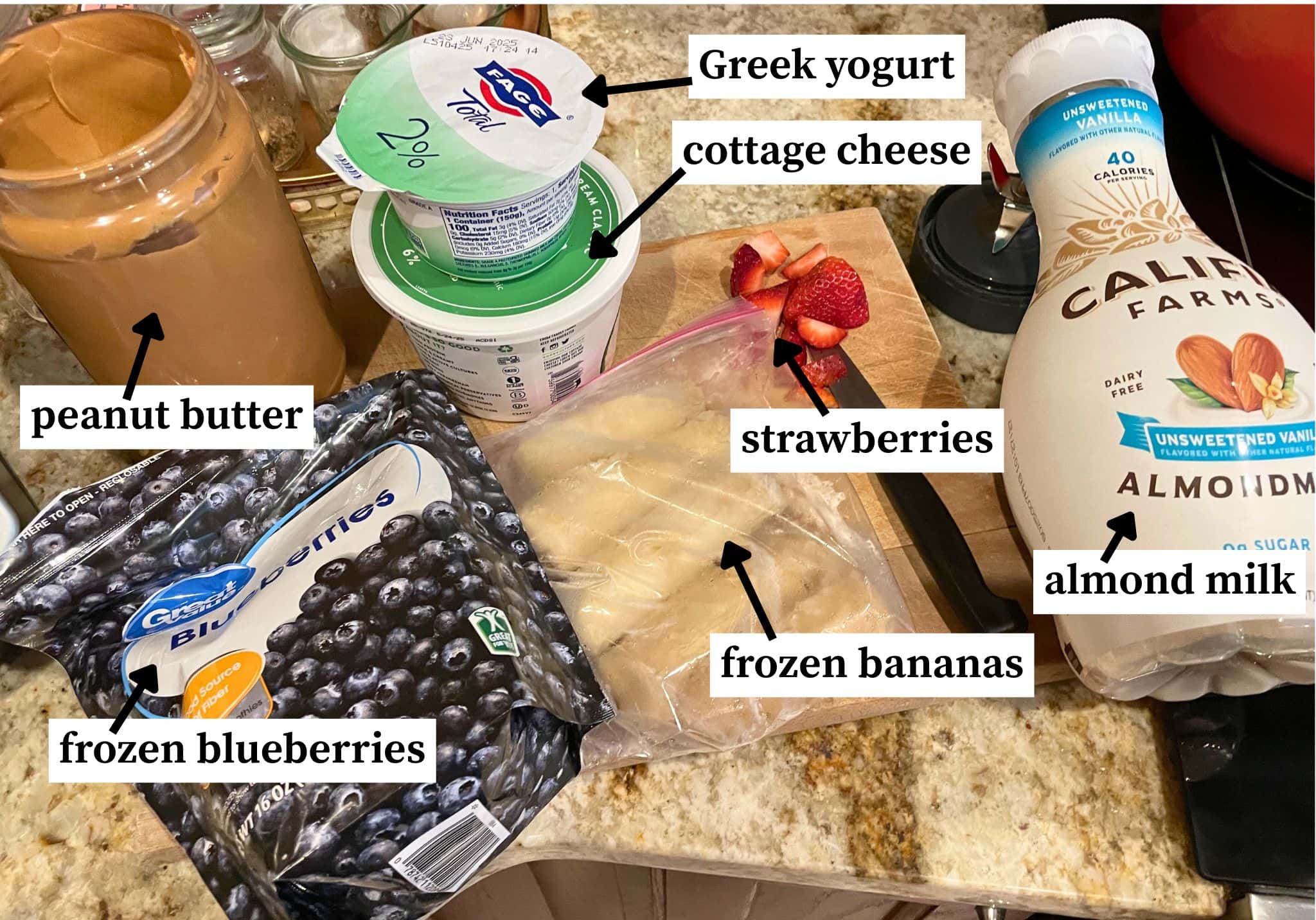 The ingredients needed to make a blueberry, banana, and peanut butter smoothie - laid out and labeled. Milk, yogurt, bananas, peanut butter, and frozen berries.