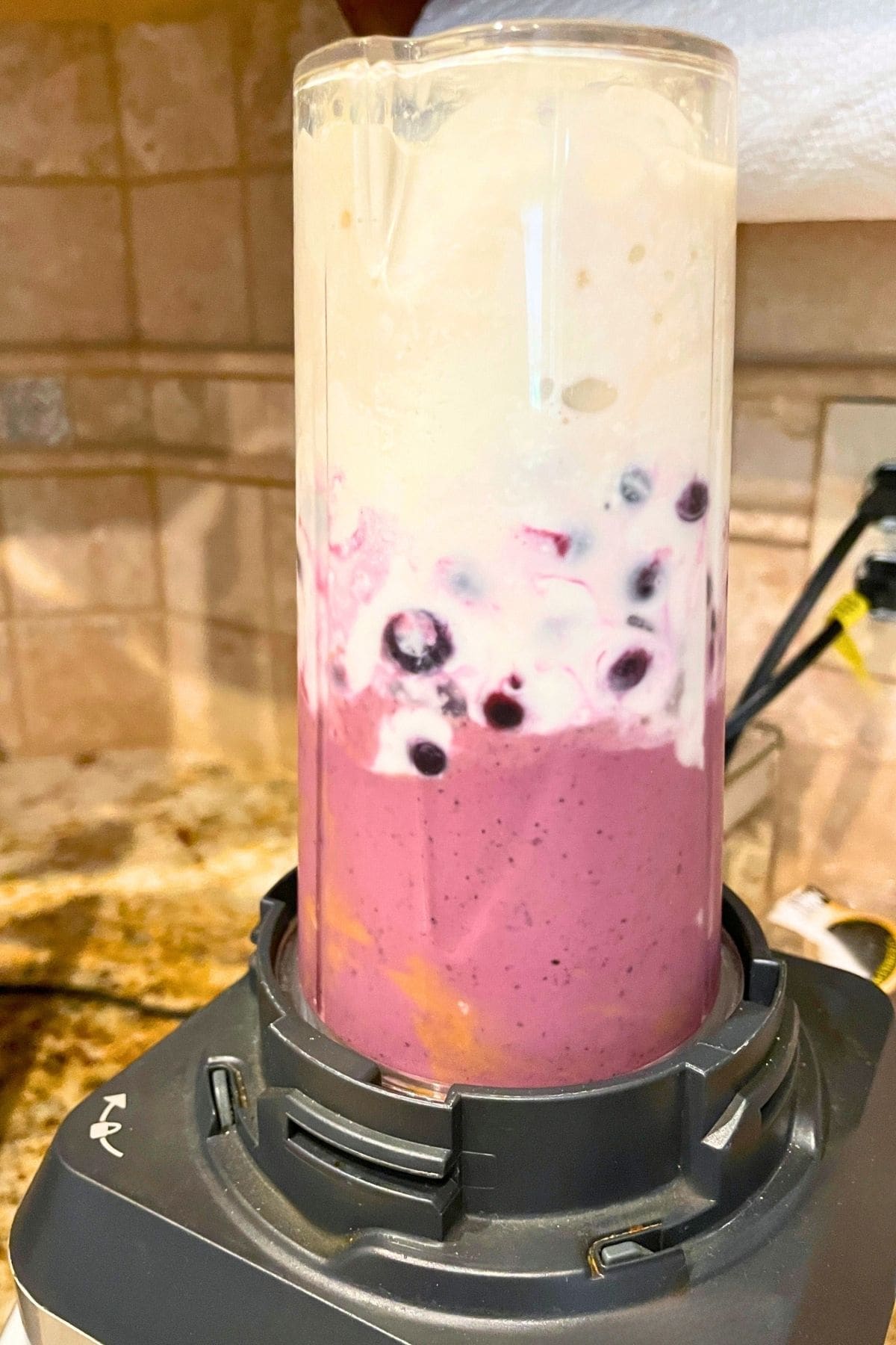 A blueberry peanut butter banana smoothie blending in a personal sized blender with the yogurt on top.