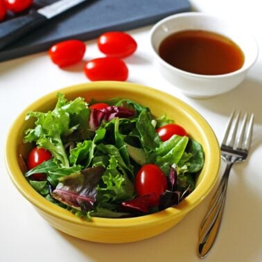 A lettuce and tomato salad in a yellow bowl with balsamic vinaigrette.